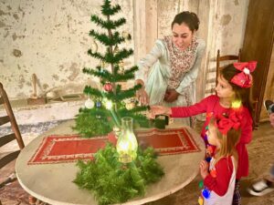 A woman in period dress looking at a christmas tree with a little girl
